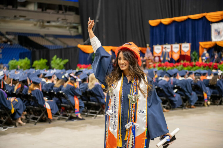 A UTSA first-generation graduate puts up the "Birds Up" hand sign after receiving her diploma at Commencement.