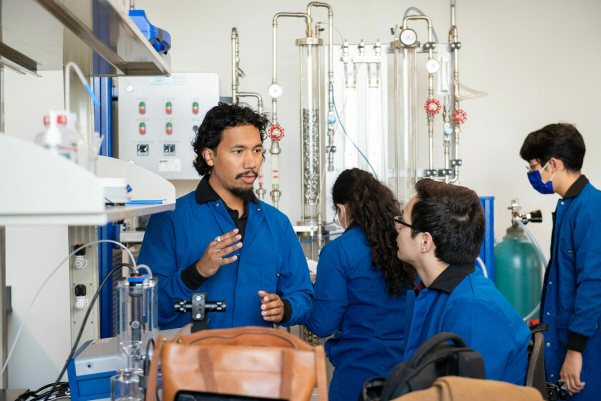 Students in blue lab coats chat in the Klesse Lab.