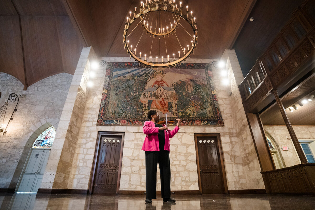 Nicole Cherry plays her violin beneath a chandelier at UTSA's Southwest Campus.