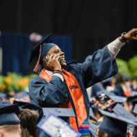 Langston Taylor stands up and points to the crowd while talking on his cellphone at Commencement.