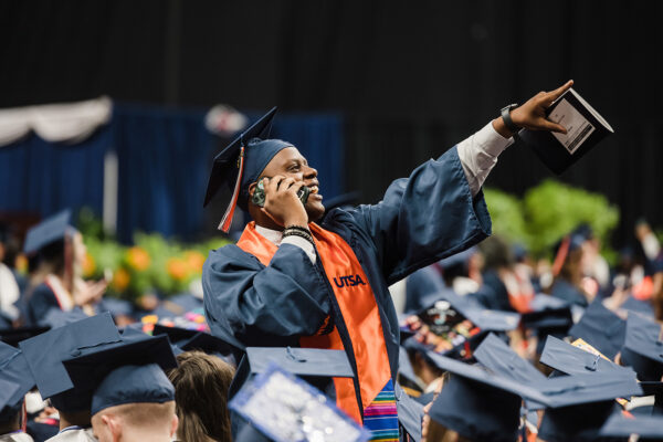 Langston Taylor stands up and points to the crowd while talking on his cellphone at Commencement.