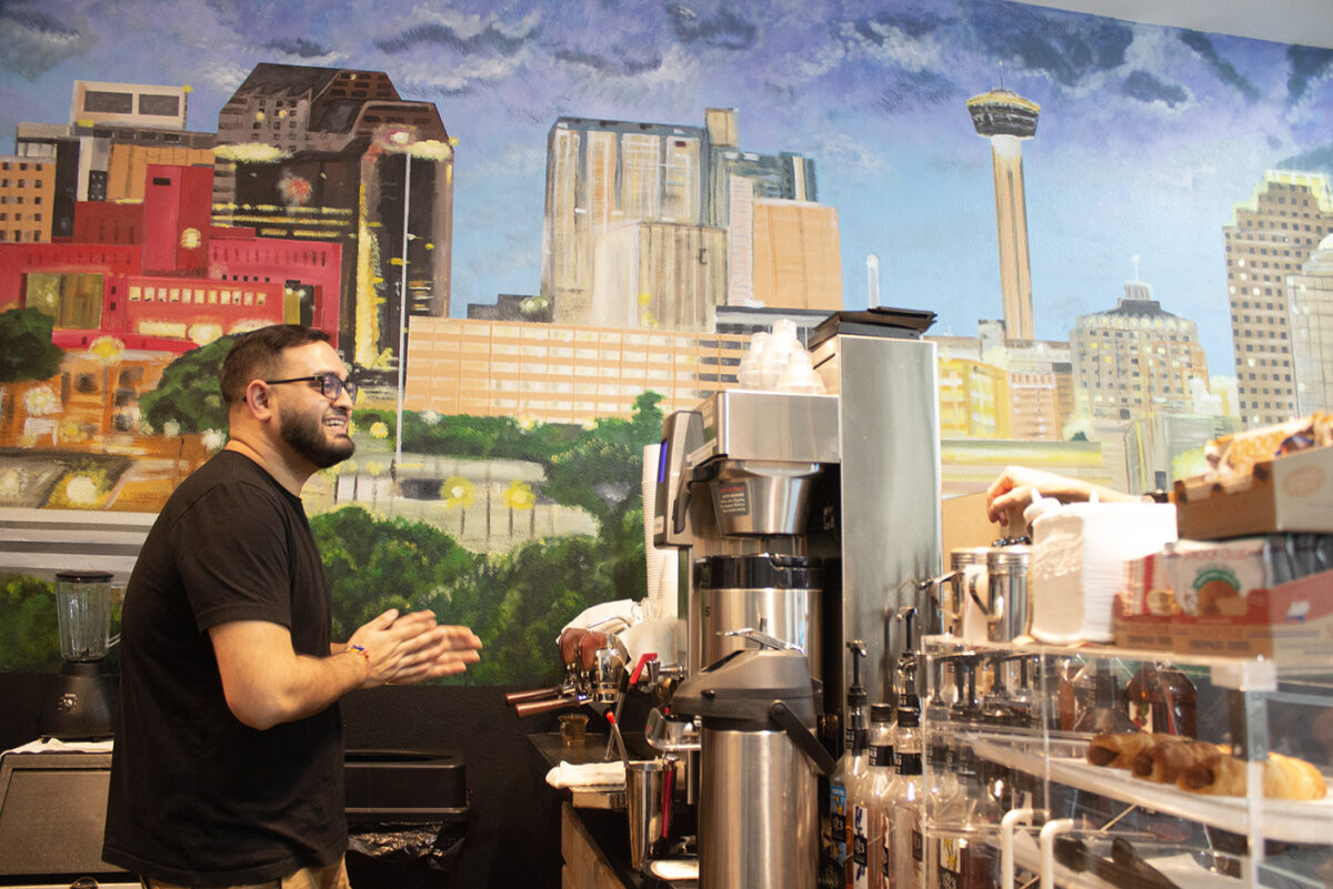 Nirav Amarnath smiles as he talks to a customer in front of a mural of the San Antonio skyline.