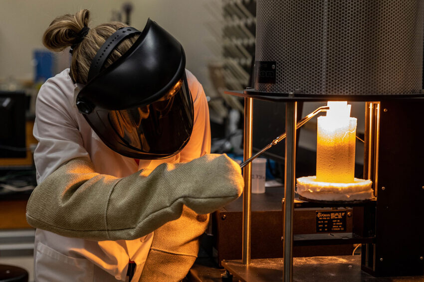 Brenna Halverson wears protective equipment as she uses utensils to grab a sample of moon lava from the laboratory furnace.