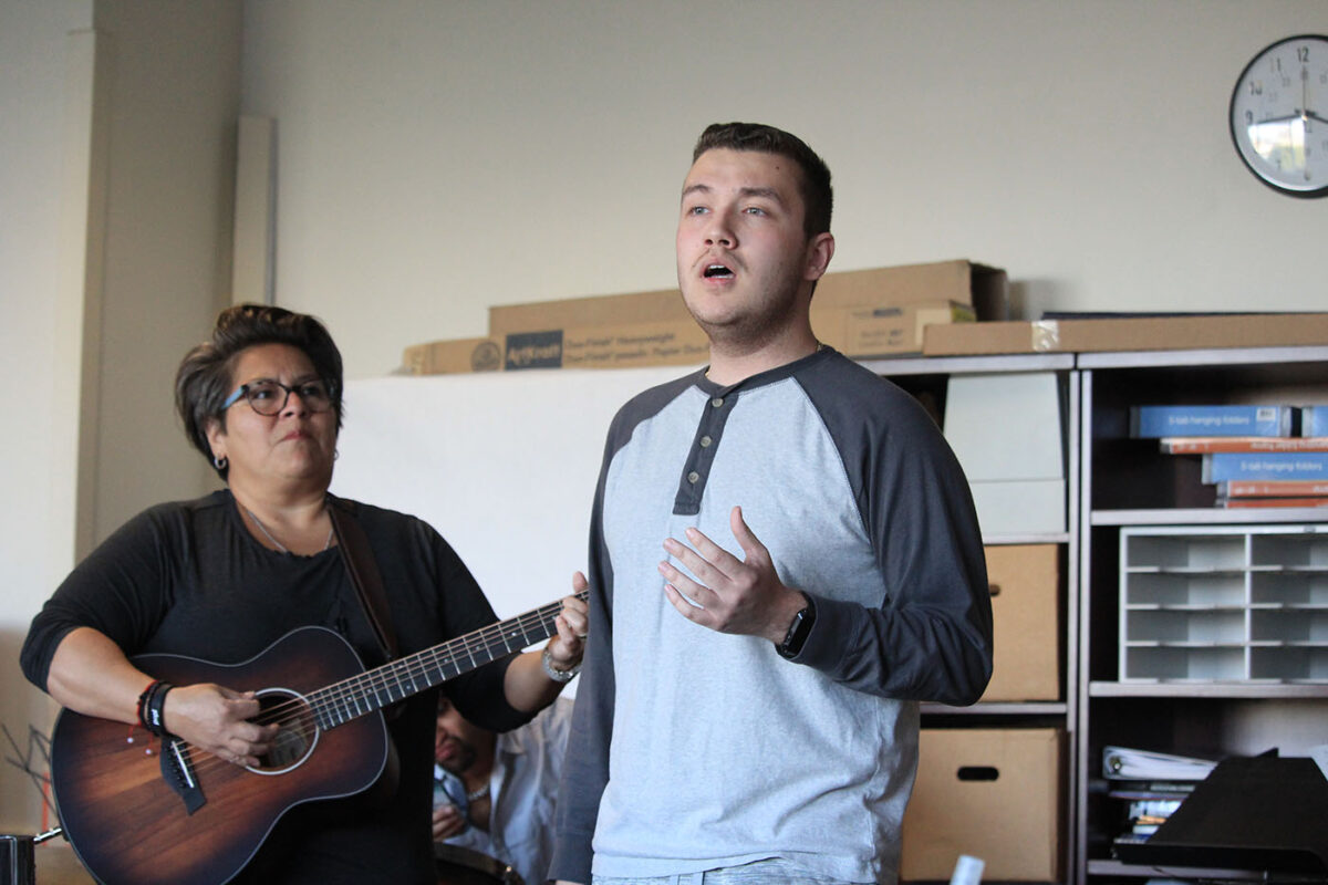 Roy Martinez sings as Rachel Cruz plays her guitar in the background.