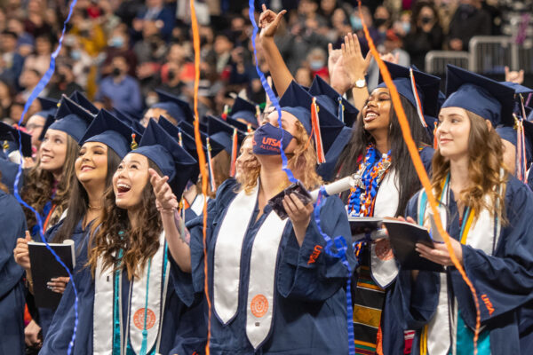 UTSA graduates celebrate as orange and blue streamers fall from the rafters.