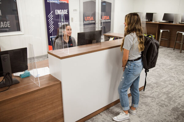 A UTSA student approaches a worker at the front desk of the Student Success Center.