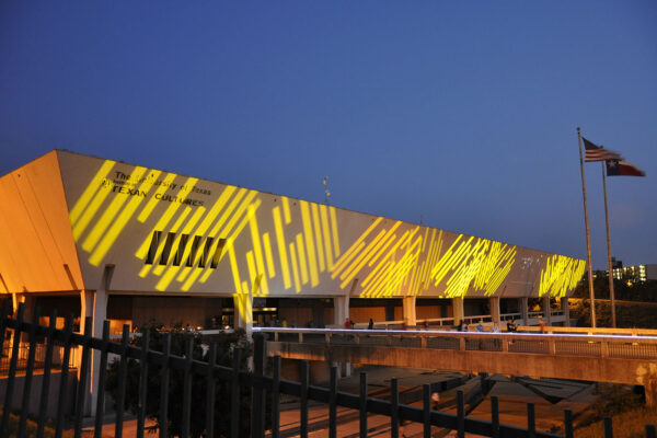 A nighttime exterior photo of the Institute of Texan Cultures with a light show being projected on the building's facade.