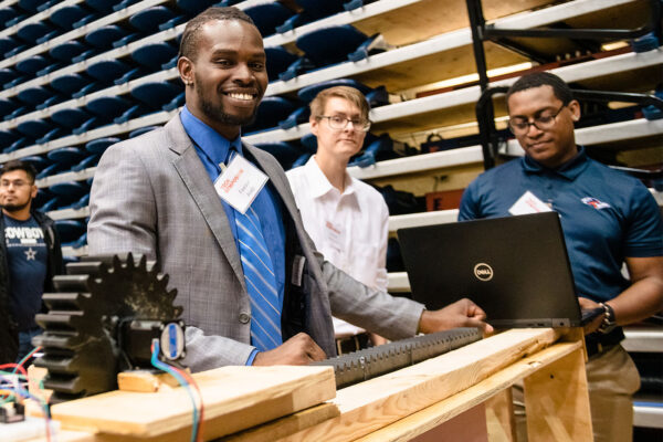 A UTSA student smiles as he shows off his group's engineering project at the Tech Symposium.
