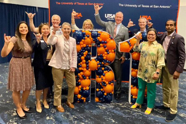 Several UTSA leaders pose for a photo with large letters spelling "R1."