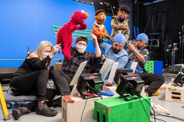 Four puppeteers control the movements of Sesame Street muppets in a studio.