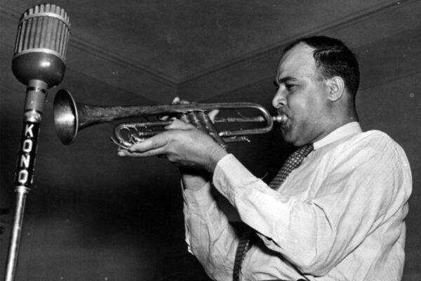 Albert “Don Albert” Dominique holds up a trumpet in front of a Kono microphone.