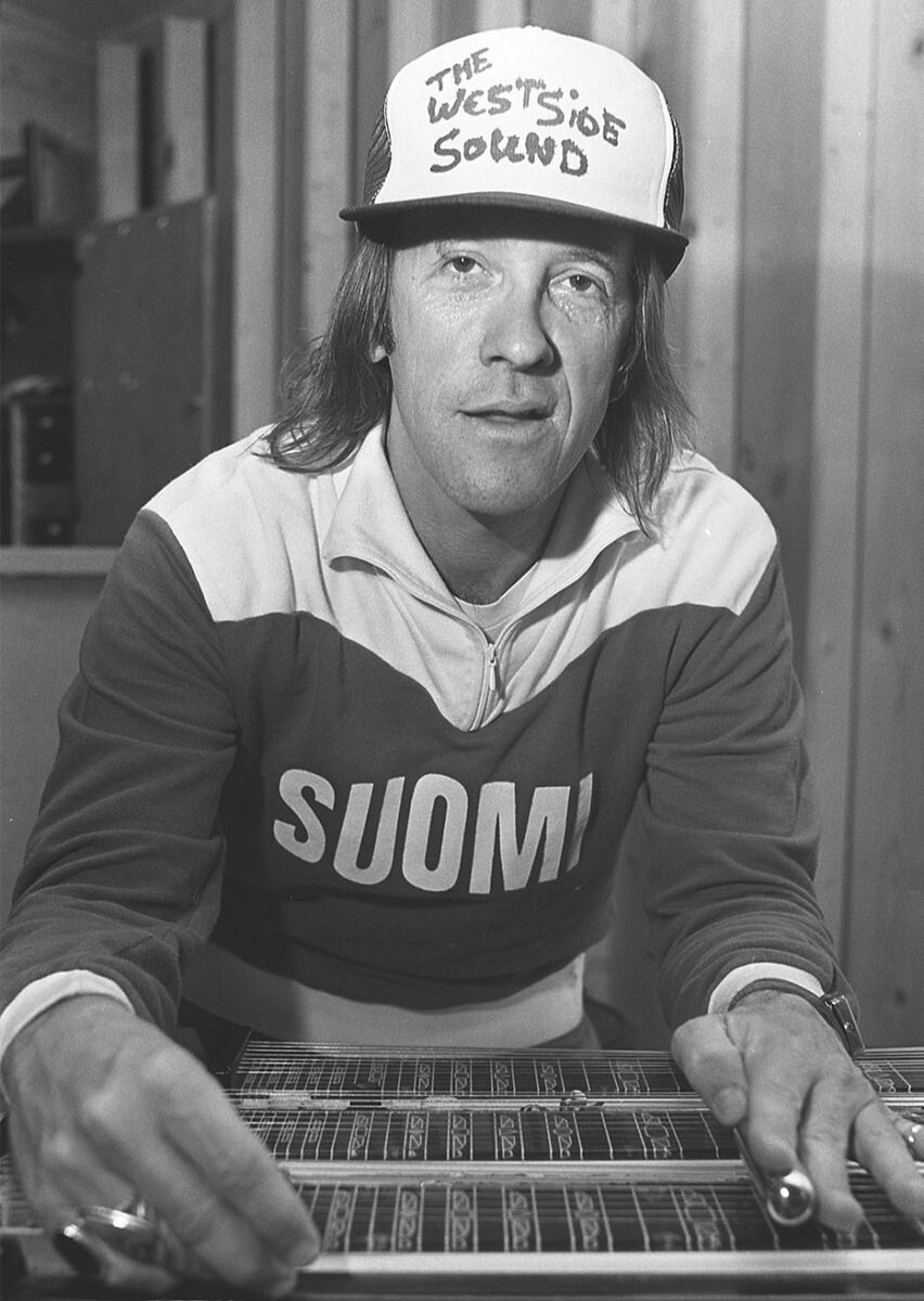 Doug Sahm plays a slide guitar in a studio while wearing a hat that reads "The Westside Sound."