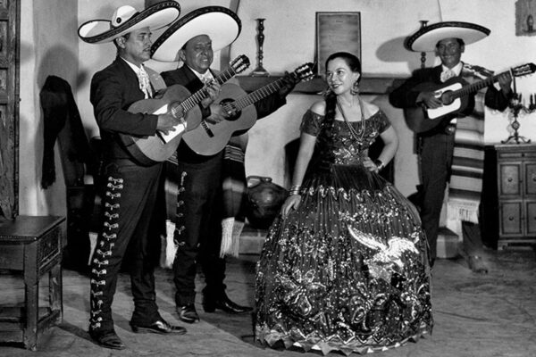 Rosita Fernandez stands in between three mariachi performers with guitars.