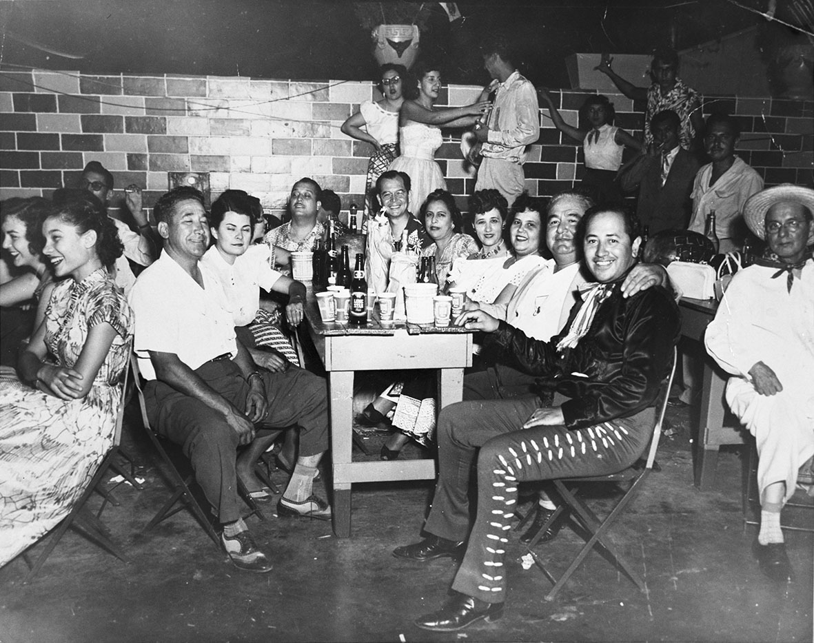 Dozens of community members sit at tables smiling and drinking while at the venue Patio Andaluz.