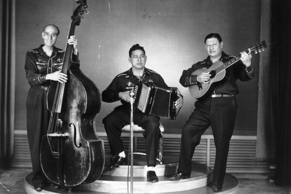 The singers of Santigago y sus Valedores stand on stage with their instruments.