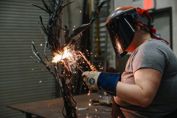 A female student uses a blowtorch to sculpt a bronze artwork