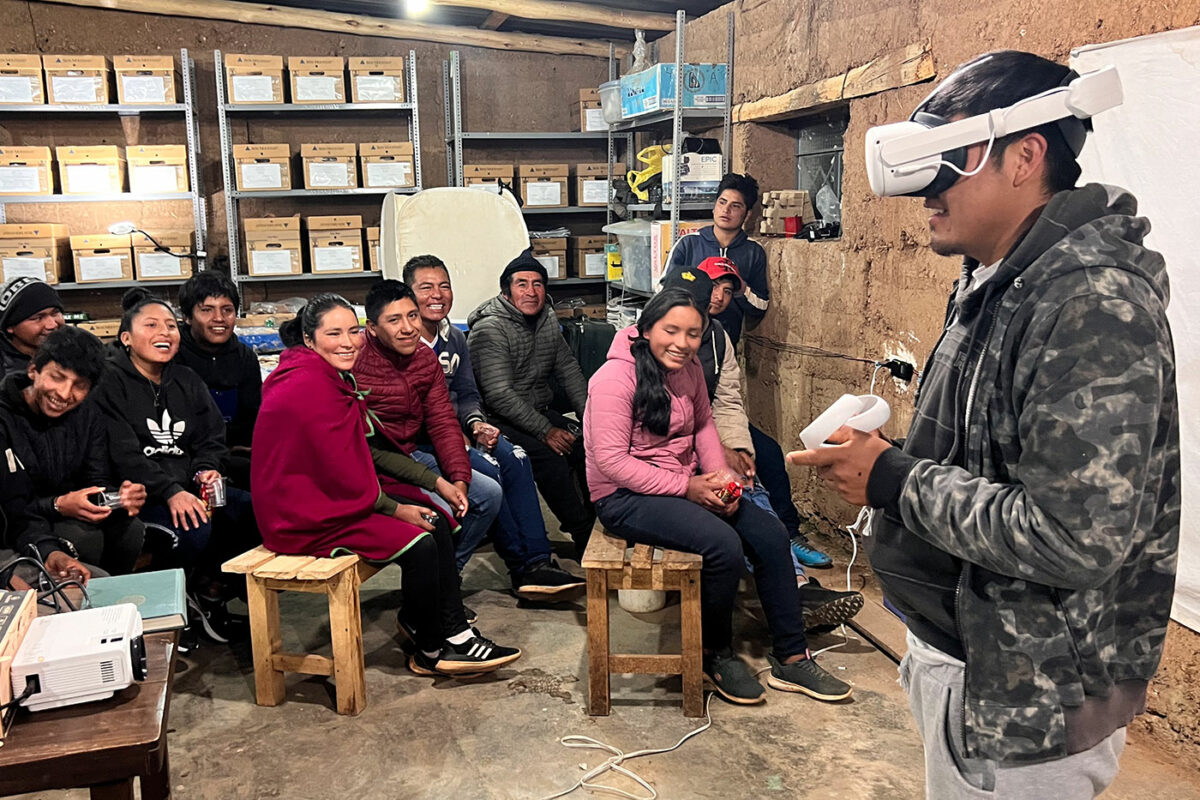 young man with VR headseat and a crowd of smiling onlookers from the village