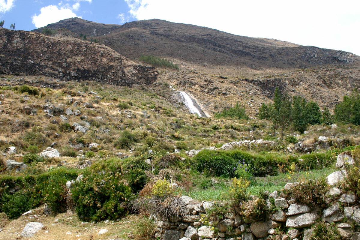 mountains with water flowing down through a natural aquaduct with ruins of ancient stone structures