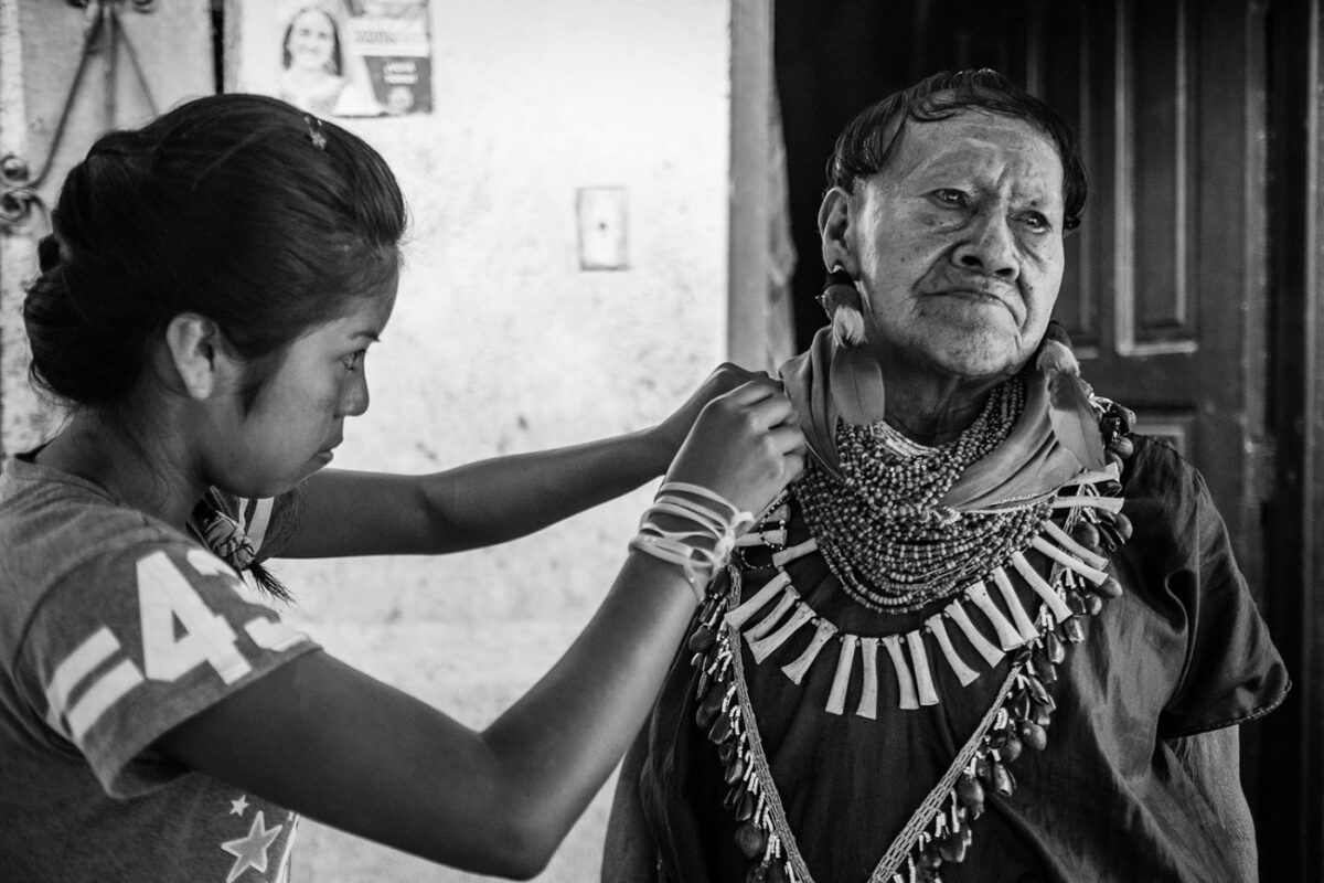 Cofán elder is dressing in traditional attire with help of teenage girl