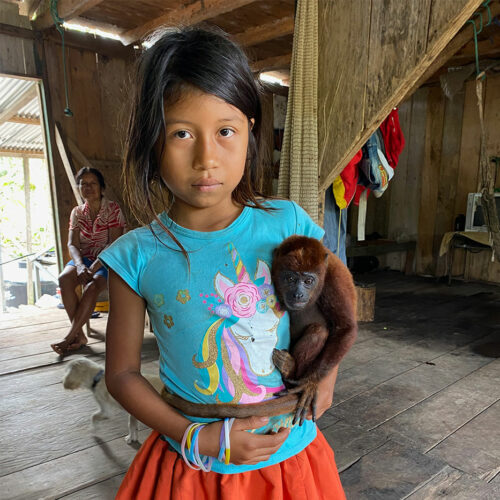 girl in wooden hut holding a small pet monkey