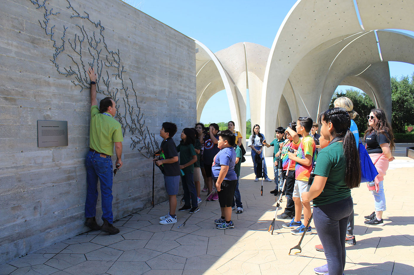 A group of students stand while listening to a guest speaker.