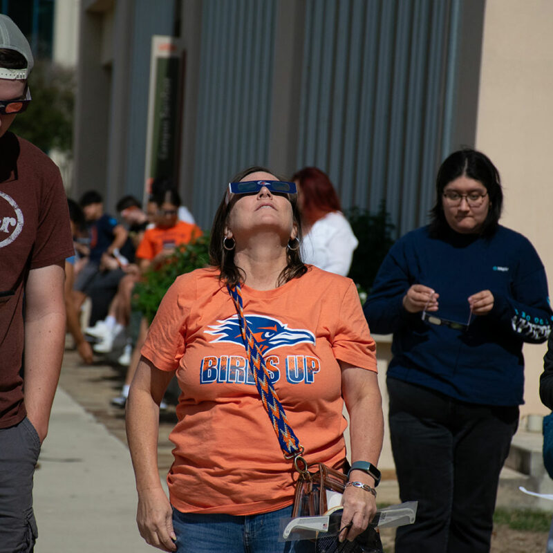 A woman looks up at the sky with solar eclipse glasses.