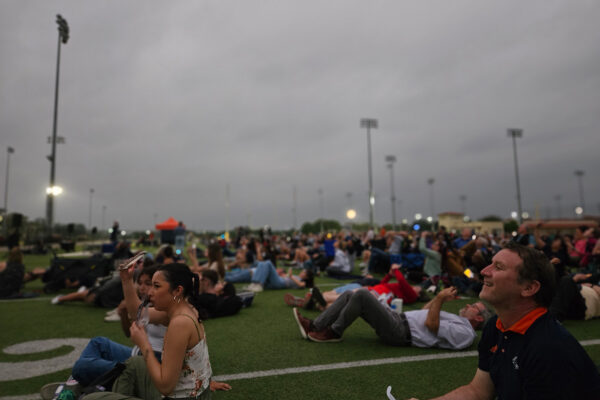 A crowd of people sit on the grass.