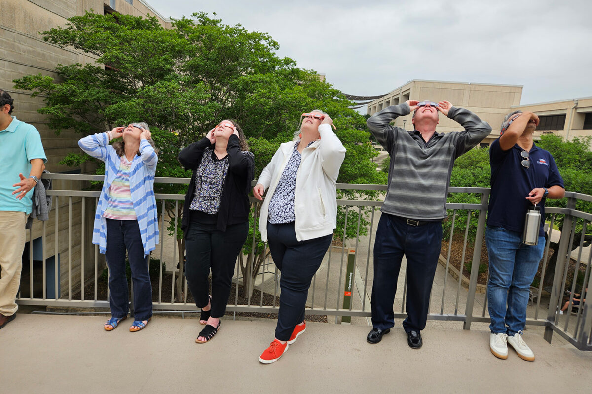 A group of faculty and staff look up at the sky.