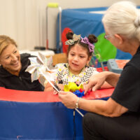 A child sits in a foam activity pool with two medical physicians.