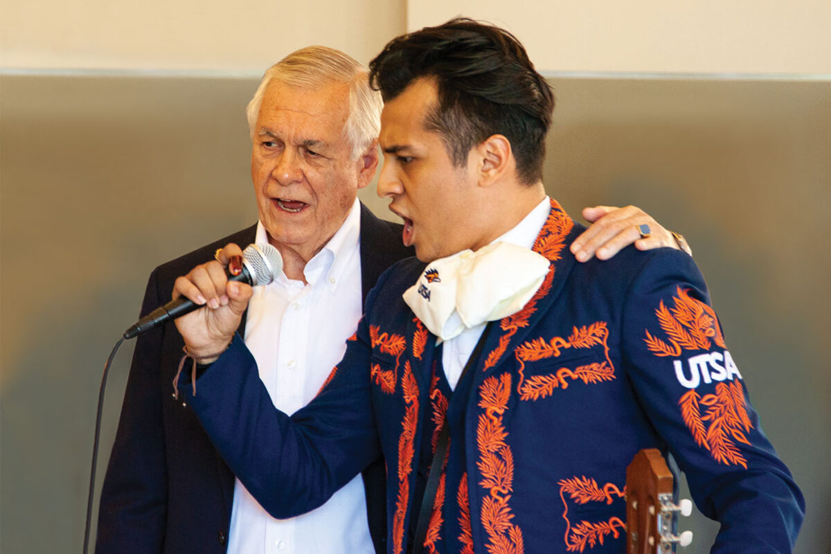 Carlos Alvarez sings into a microphone with a UTSA mariachi singer