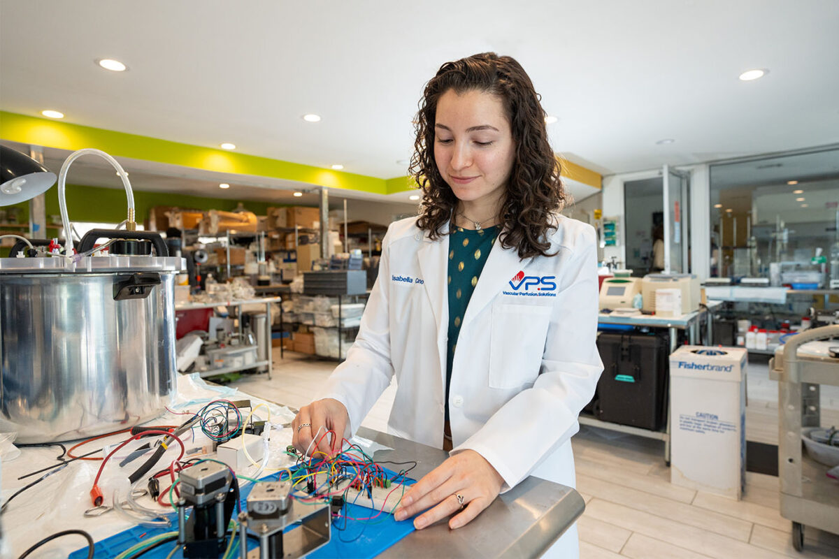 Isabella Cano adjusts electrical wires hooked to a device in a laboratory