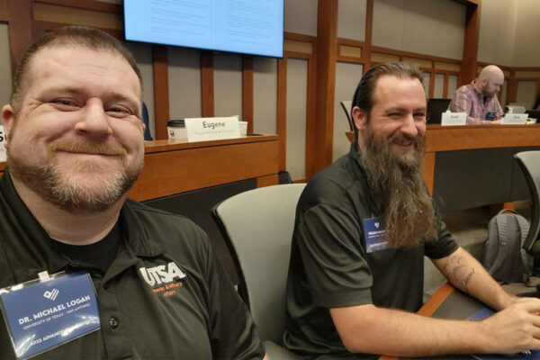 Michael Logan and William Lansdon take a selfie while sitting at a symposium