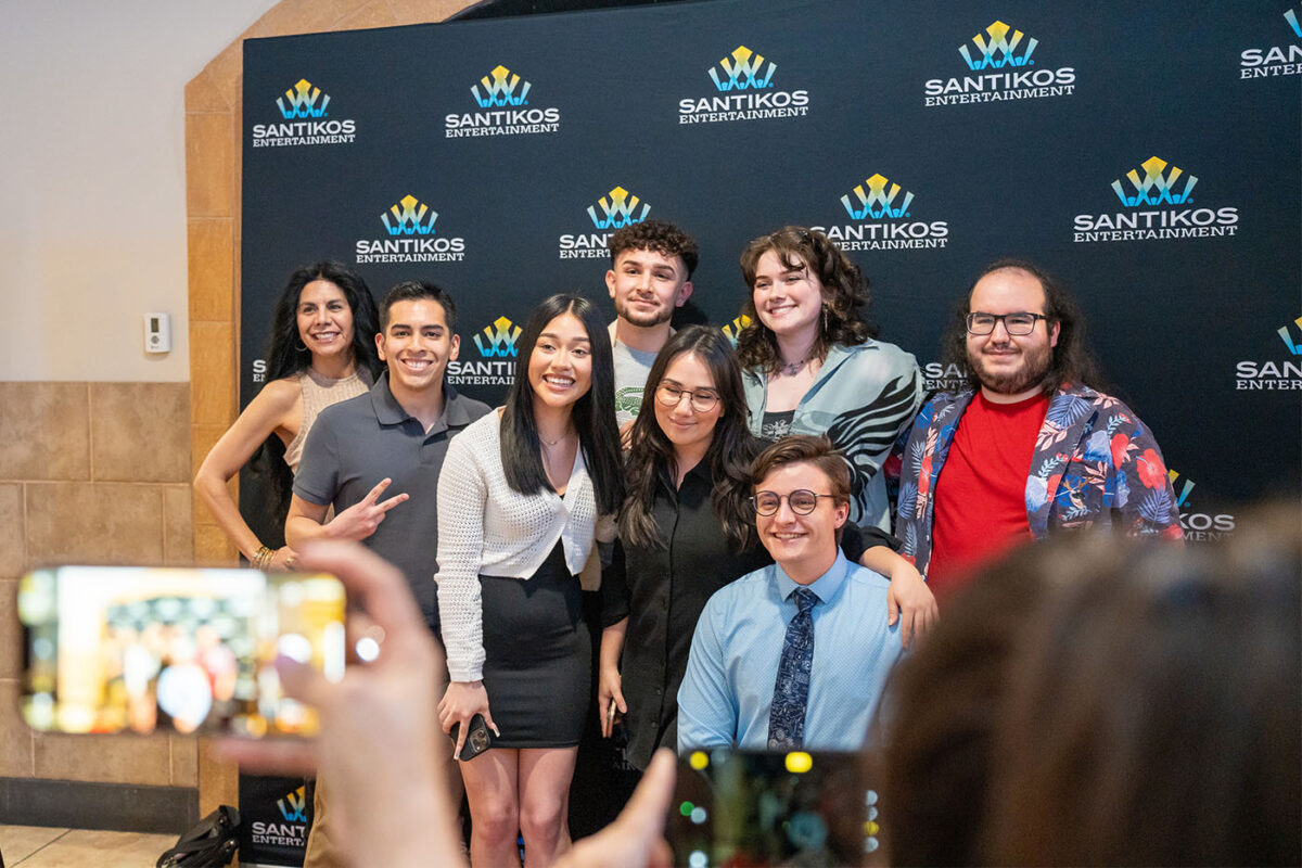 Eight people pose for photos in front of a backdrop with the Santikos logo