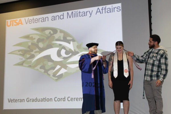 UTSA's Michael Logan places a ceremonial cord over the back of a student-veteran's neck