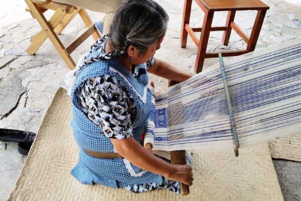 Indigenous woman weaving on knees in open air area