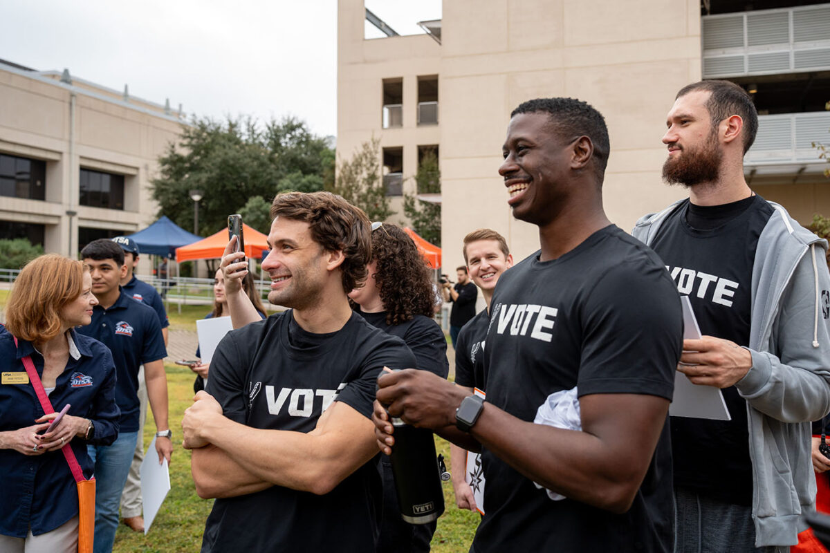 Spurs players and staffers smile while watching their teammates pose for photos.