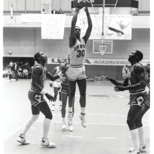 Man jumps in air with basketball.