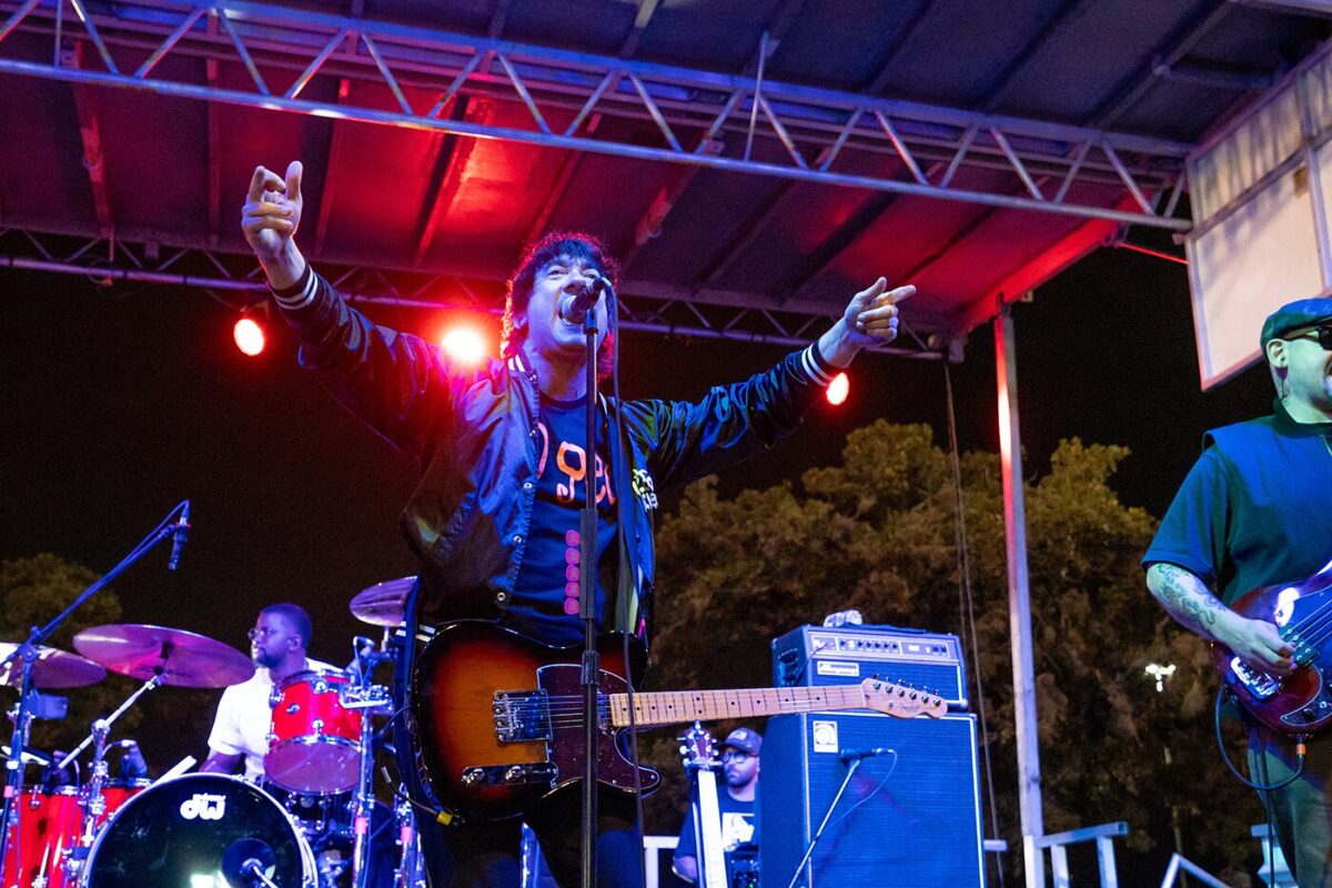 Man raises arms up as he sings into microphone.