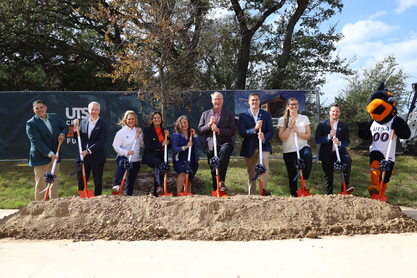 10 people dip their shovels into a mound of dirt