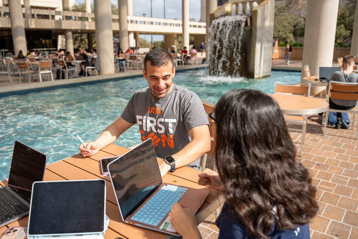 Two students sit in front of laptops at a table