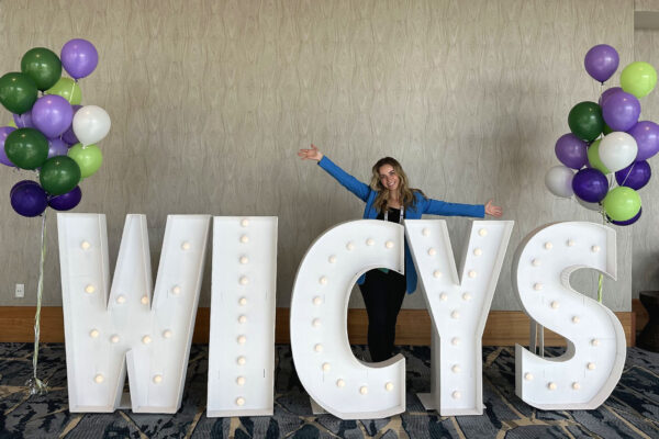 Katie Thomas smiles from behind giant letters spelling "WICYS."