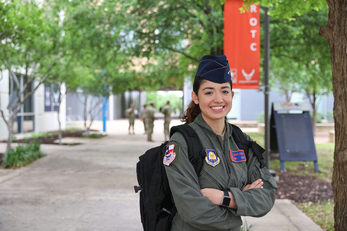 An Air Force ROTC cadet smiles with her arms folded in front of an orange ROTC banner
