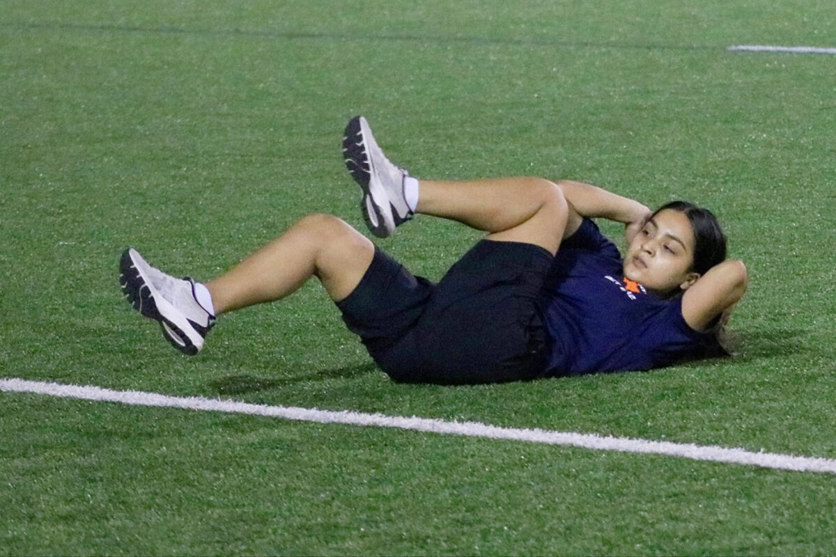 A female cadet does stomach crunches on the field.