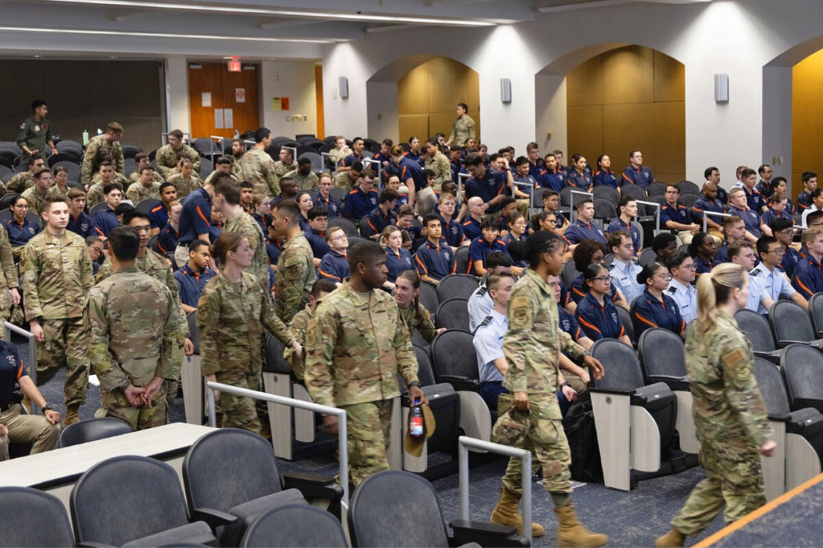 Various cadets gather in an auditorium. Some are in blue polos and others are in full camoflauge uniforms.
