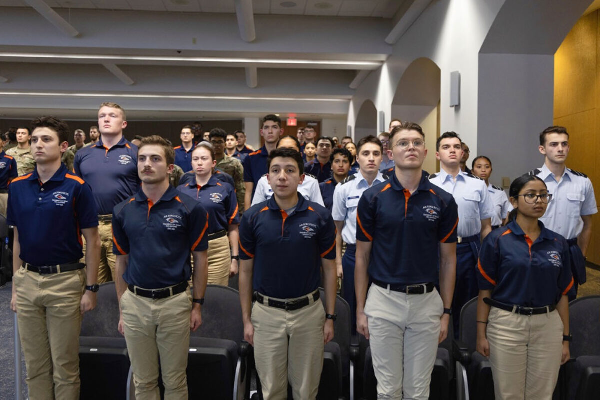 The cadets in the auditorium stand at attention.