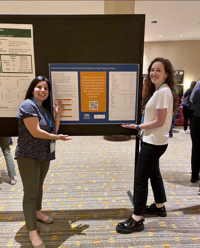 Two women stand beside a poster.