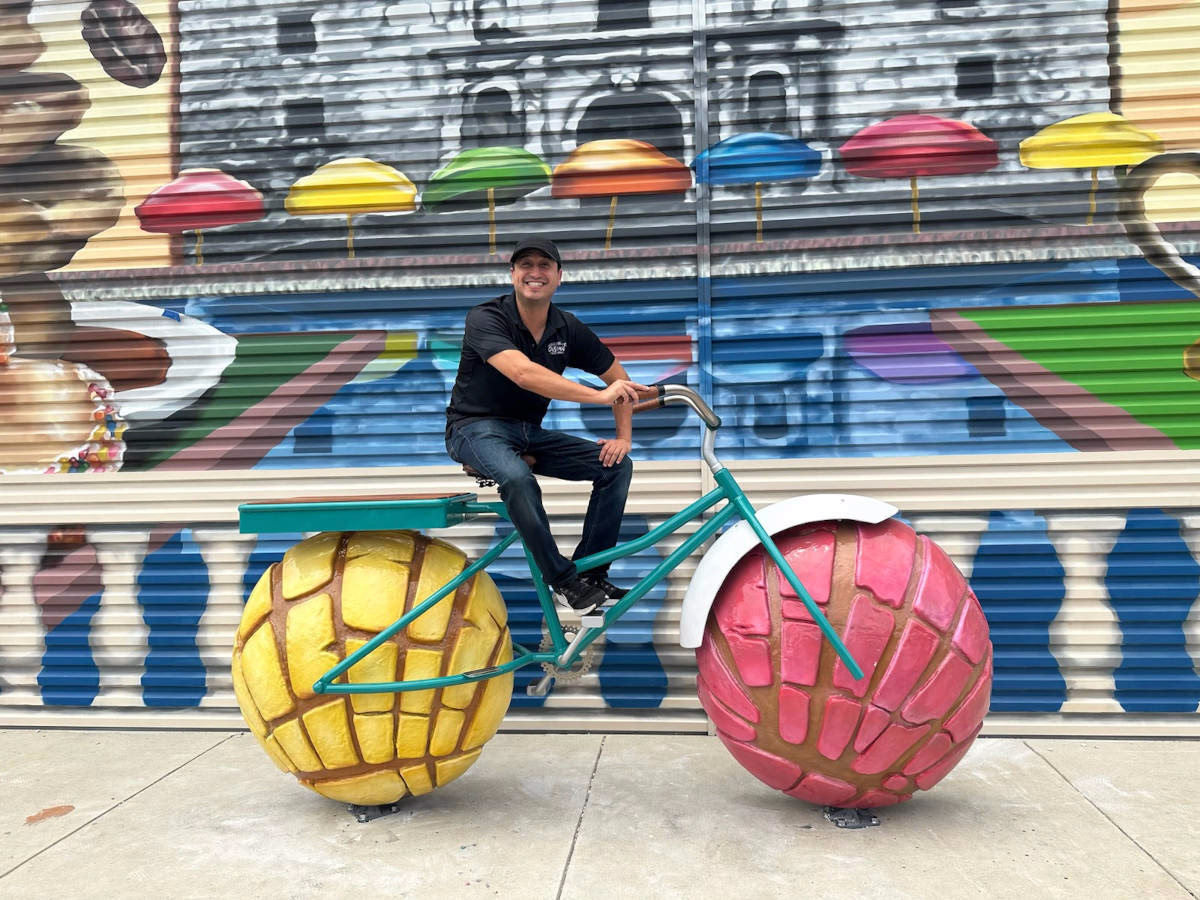 A man sits on top of a metal bike, which has wheels with pastries.
