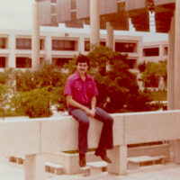 A man in a red shirt sits on top of a concrete wall.