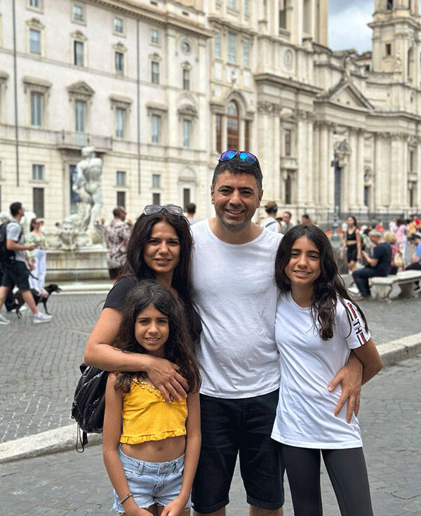 A man, woman, and two young girls stand beside each other and hug.