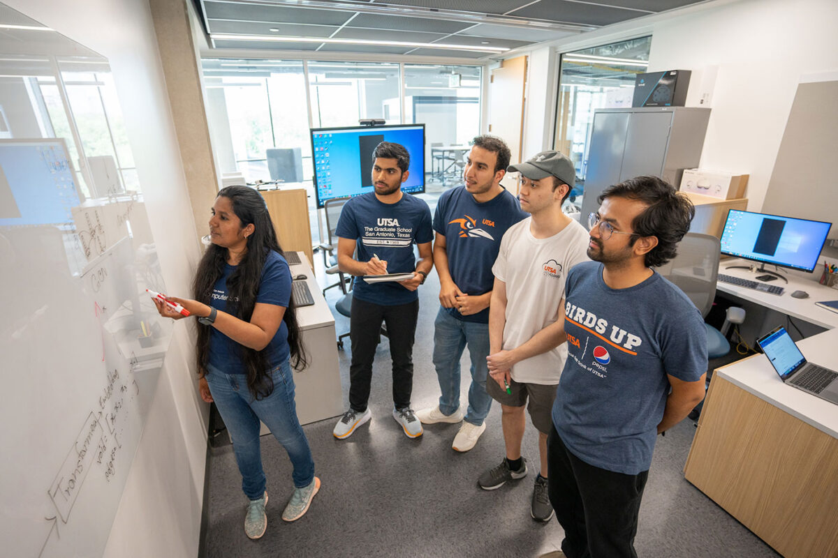 Several students look at another individual who is writing on a white board.